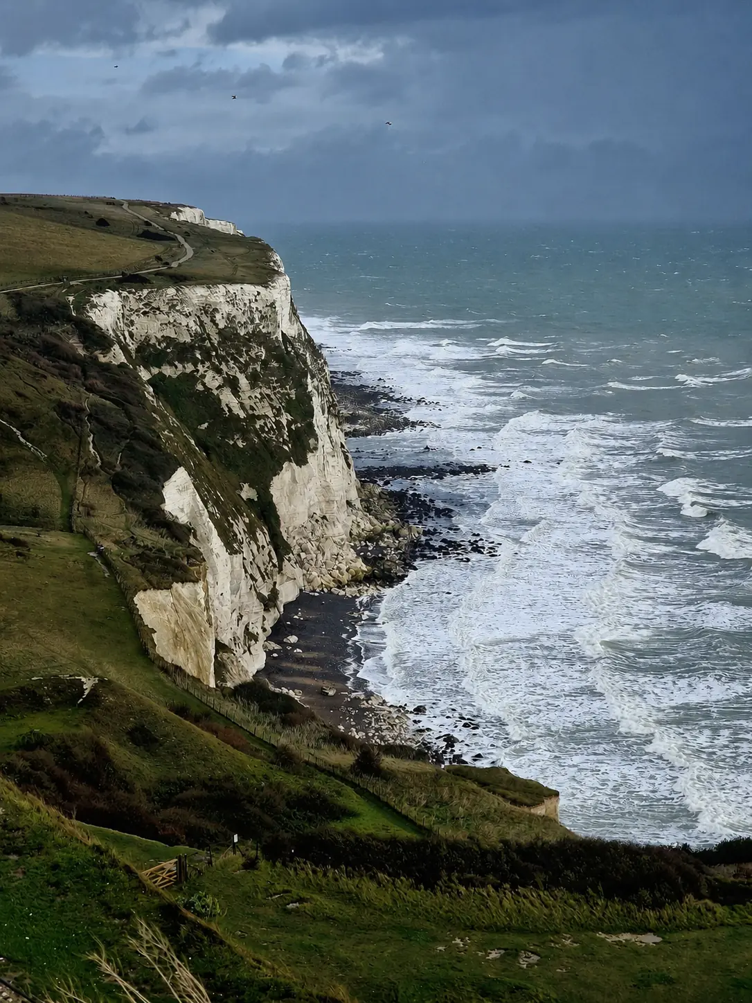 White coastal cliffs above rough sea beneath storm clouds