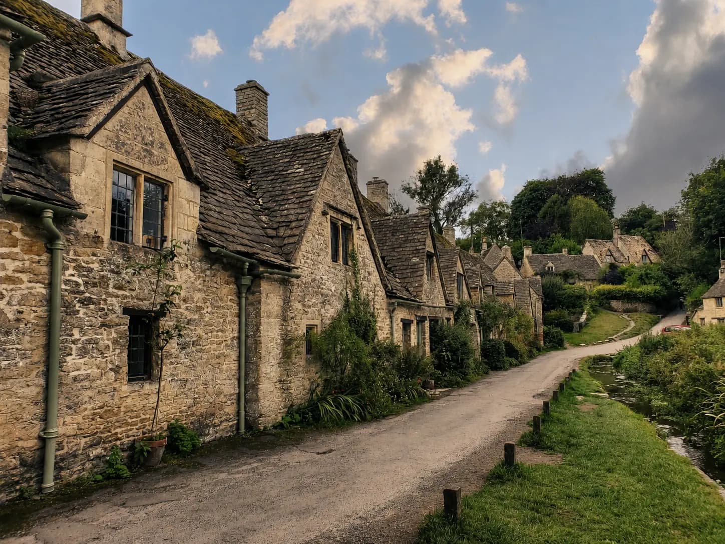 Stone cottages beside a winding village lane under a cloud-filled sky